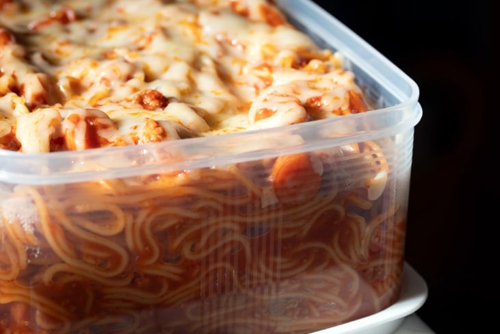 Filipino spaghetti with melted cheese on top in a plastic food tub container