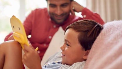 Father And Son At Home On Sofa In Lounge Playing With Digital Tablet Or Electronic Toy Together