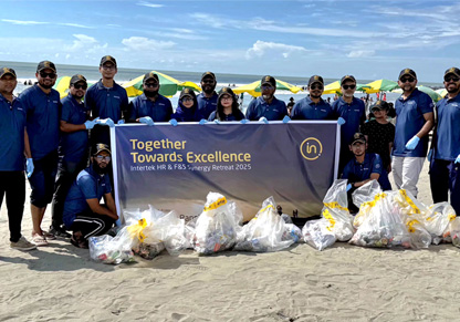 A group of 15 Intertek colleagues wearing dark blue tops and Intertek hats stand on a beach with the rubbish they have collected, with a sign that says "Together Towards Excellence". 