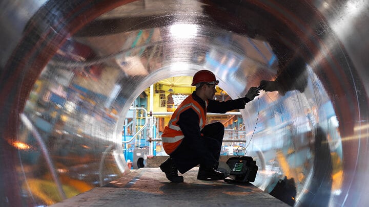 Industrial worker using machine inside of a large pipe