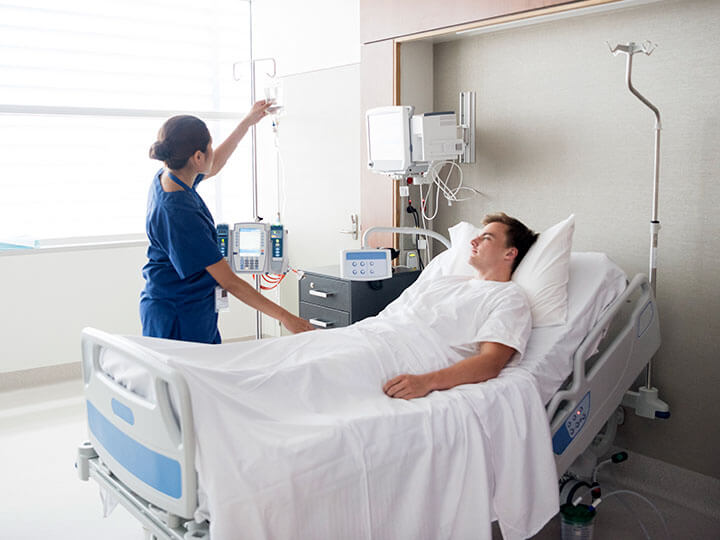 young adult male lying in a hospital bed being attended to by female hospital staff member