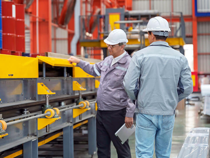 Industrial consultant discussing project with engineer, both wearing hardhats in an industrial manufacturing plant