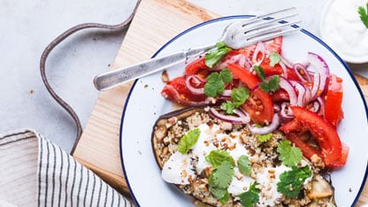 Healthy plate of food with quinoa, eggplant, tomato, red onion, and cilantro