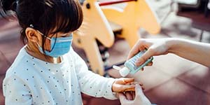 Asian child in blue facemask getting hand sanitizer put in her hand