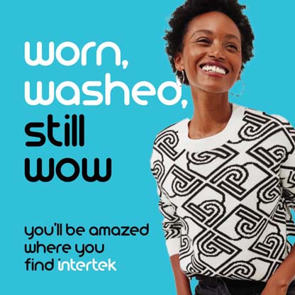A woman smiling while wearing a white sweater with a distinct graphic pattern
